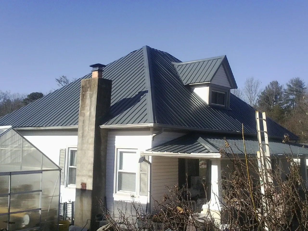 Dark blue standing seam metal roof on a white farmhouse with dormer — Slate & Tile Roof Repair by Roofing Brothers in Jewett