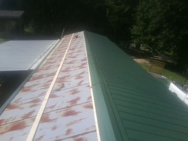 Old rusted panels beside newly installed green metal roofing — Wind Damage Roof Repair by Roofing Brothers in Jewett