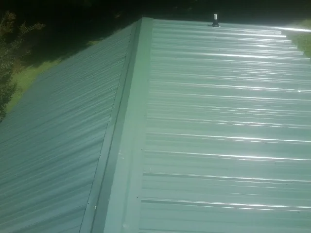 New green metal panels meeting at the ridge of a roof — Flat Roof Repair work by our crew in Jewett