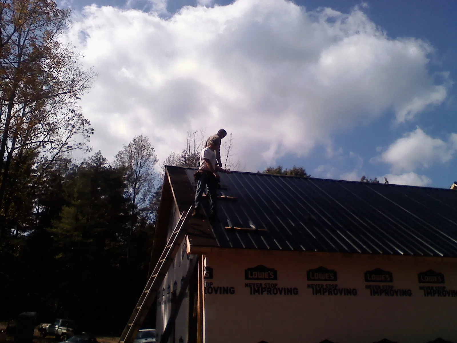 Roofer fastening dark metal panels high against a cloudy sky, from a Roof Inspection job in Jewett