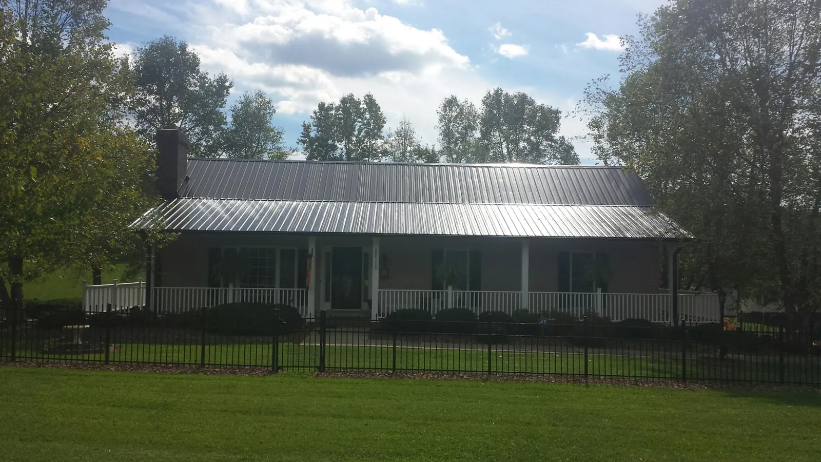 Gray metal roof on a brick ranch with a full width front porch — Gutter Guard Installation work by our crew in Jewett