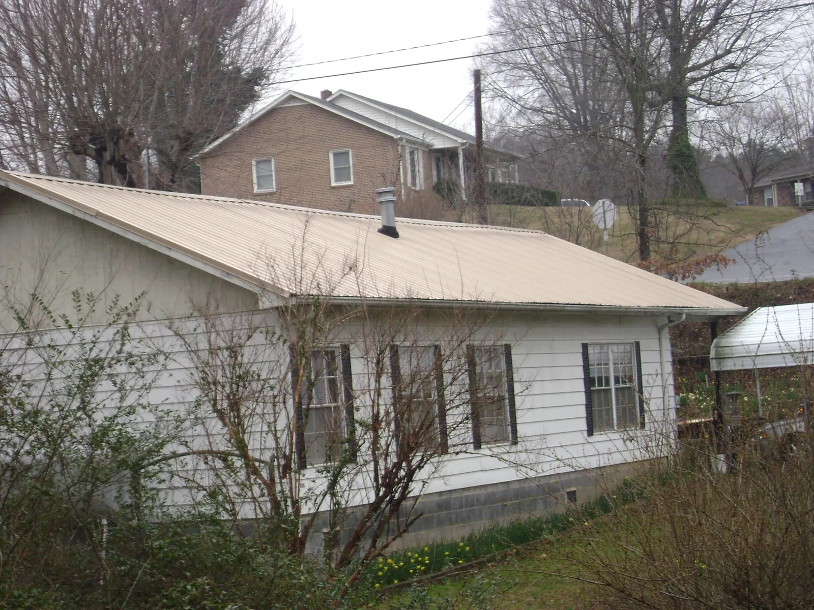 Tan metal roof on a white sided house set into a hillside — Commercial Roofing by Roofing Brothers in Jewett