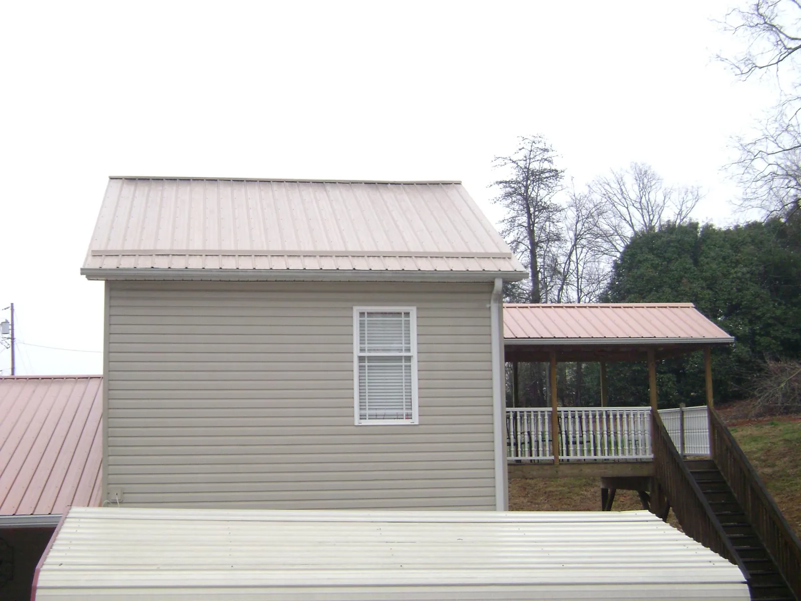 Tan metal roofs on a two story addition and attached porch, from a Roof Replacement job in Jewett